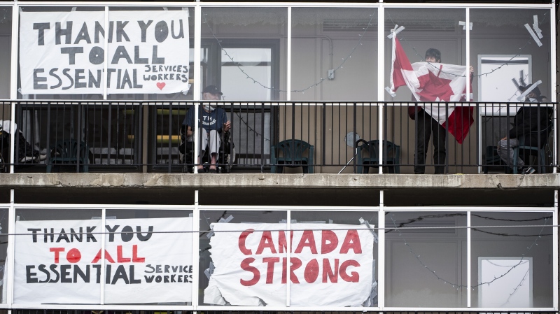 A resident untangles a Canadian flag in order to tape it back up to the window on a balcony at the Laurier Manor in Ottawa, a long term care facility experiencing an outbreak of COVID-19, on Sunday, April 26, 2020. (THE CANADIAN PRESS/Justin Tang)